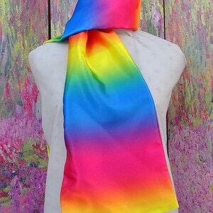 May include: A multi-coloured scarf, draped over a mannequin. The scarf fades from blue to pink, orange, and yellow. The fabric has a silky appearance and a subtle sheen. A vibrant accessory.