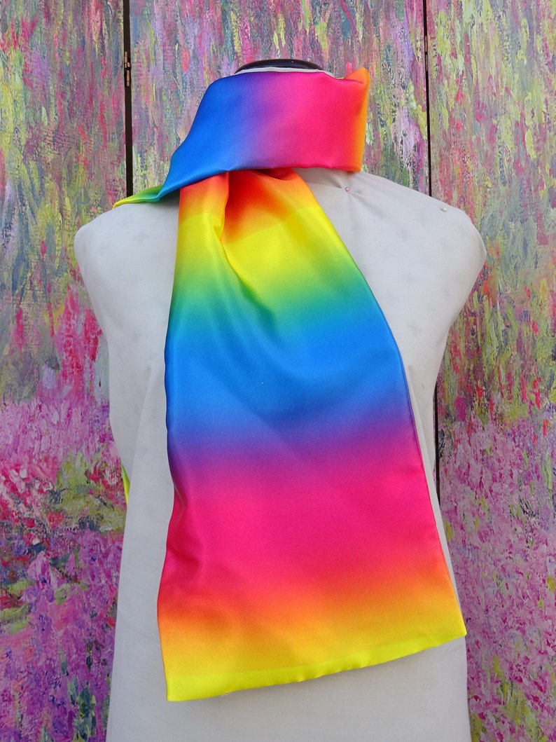 May include: A multi-coloured scarf, draped over a mannequin. The scarf fades from blue to pink, orange, and yellow. The fabric has a silky appearance and a subtle sheen. A vibrant accessory.
