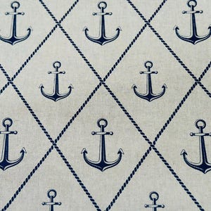 May include: A light beige fabric featuring a repeating pattern of dark navy blue anchors centered within a diamond grid formed by thin, dark navy blue rope-like lines. The anchors are evenly spaced throughout the textile design.