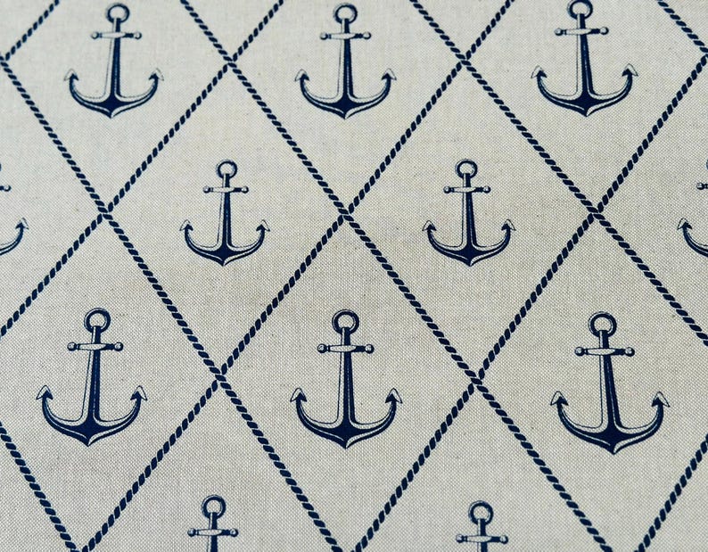 May include: A light beige fabric featuring a repeating pattern of dark navy blue anchors centered within a diamond grid formed by thin, dark navy blue rope-like lines. The anchors are evenly spaced throughout the textile design.