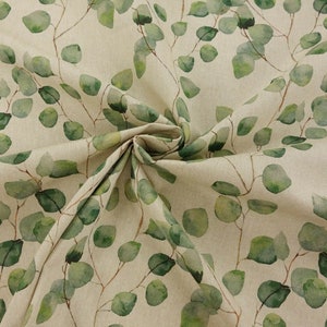 Puede incluir: Tela con un diseño de hojas de eucalipto en acuarela. Las hojas son de color verde suave con tallos marrones, sobre un fondo beige. La tela está doblada, mostrando su textura y diseño.