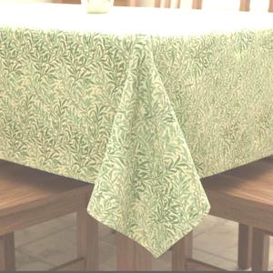 Op de afbeelding: Een rechthoekig tafelkleed met een botanische all-over print van overlappende wilgenbladeren in diverse tinten salie-, olijf- en bosgroen op een lichtcrème achtergrond, gedrapeerd over een tafel met een zichtbare hoekplooi.
