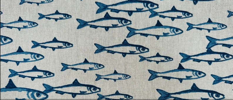 May include: A light beige fabric featuring a repeating pattern of dark blue fish illustrations. The fish are oriented in various directions, creating a school-like effect across the textured surface of the textile material.