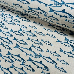 May include: A roll of off-white fabric featuring a repeating pattern of dark blue fish printed in various sizes and orientations. The textile has a visible woven texture, and the fish illustrations are rendered in a simple, clean style.