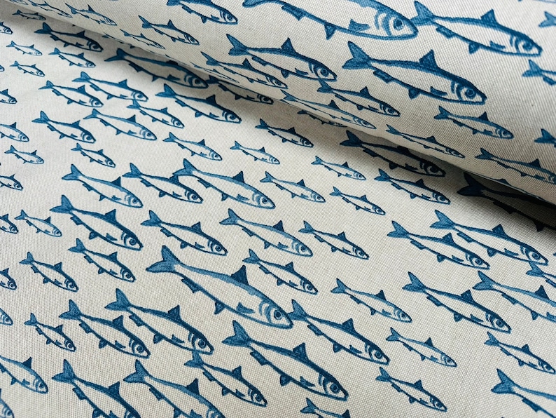 May include: A roll of off-white fabric featuring a repeating pattern of dark blue fish printed in various sizes and orientations. The textile has a visible woven texture, and the fish illustrations are rendered in a simple, clean style.