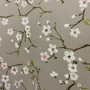 Könnte beinhalten: Ein Stoff mit einem sich wiederholenden Muster aus weißen Kirschblüten mit rosa Zentren und grünen Blättern auf braunen Zweigen. Die Zweige sind vor einem hellgrauen Hintergrund angeordnet.
