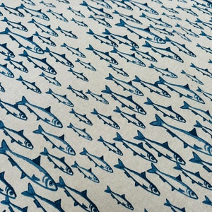 May include: A light beige fabric featuring a repeating pattern of dark blue fish illustrations. The fish are oriented in various directions, creating a school-like effect across the textile surface with consistent ink-style detailing.
