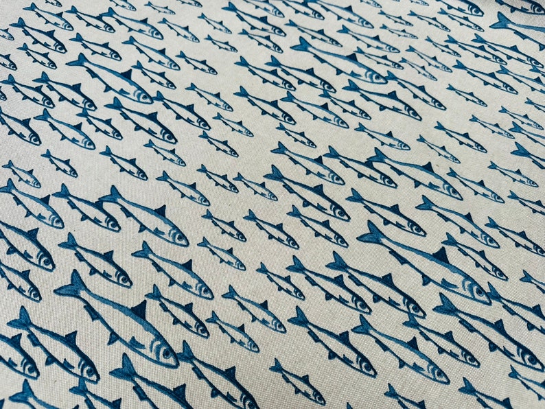 May include: A light beige fabric featuring a repeating pattern of dark blue fish illustrations. The fish are oriented in various directions, creating a school-like effect across the textile surface with consistent ink-style detailing.
