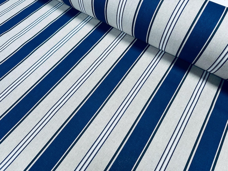 May include: A roll of fabric featuring a repeating pattern of wide navy blue stripes alternating with light gray sections. Each light gray section contains a central thin navy blue stripe flanked by two even thinner white lines, creating a classic striped design.