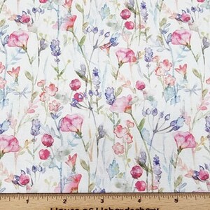May include: Fabric with a floral watercolour design. The pattern features pink, purple, and blue flowers and foliage on a white background. The fabric has a delicate feel, with a ruler at the bottom.