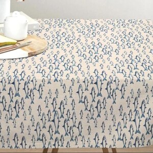 May include: A rectangular tablecloth featuring a repeating pattern of small, dark blue fish printed on a light beige fabric. The fish are oriented in various directions across the surface, creating a dense, uniform design throughout the textile.