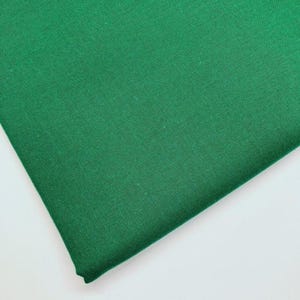 Pode incluir: Um pedaço de tecido verde liso dobrado. O tecido tem uma aparência ligeiramente texturizada e é um tom vibrante de verde. O tecido é dobrado sobre si mesmo, criando um efeito em camadas. O fundo é branco.