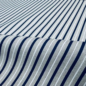 May include: A woven fabric featuring a repeating pattern of bold navy blue vertical stripes alternating with thinner white stripes against a textured light gray background. The material is folded to show the depth and weave of the textile.