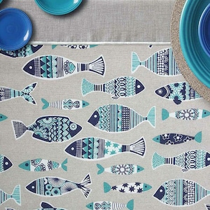 Peut inclure: Une nappe grise avec un motif répété de poissons stylisés dans des tons de bleu et de turquoise. Les poissons présentent des motifs complexes et sont disposés en différentes tailles et orientations. Des assiettes bleues sont visibles en haut.