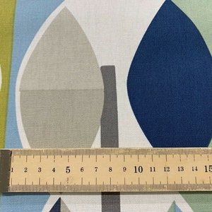 May include: Close-up of a fabric with a leaf-like pattern in shades of blue, green, grey, and white. A wooden ruler with centimetre markings is placed across the fabric, measuring up to 17 cm, or approximately 6.7 inches.