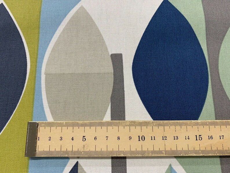 May include: Close-up of a fabric with a leaf-like pattern in shades of blue, green, grey, and white. A wooden ruler with centimetre markings is placed across the fabric, measuring up to 17 cm, or approximately 6.7 inches.