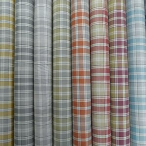 May include: Several rolls of fabric with different plaid designs. The colours range from green and grey to red and blue. The material looks like cotton or a similar fabric, ideal for clothing or home furnishings. Each roll is tightly wound.