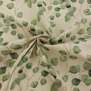 May include: Fabric featuring a watercolour eucalyptus leaf design. The leaves are soft green with brown stems, set against a beige backdrop. The fabric is folded, revealing its texture and pattern.