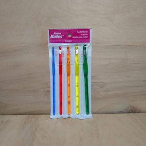 May include: A package of Susan Bates Crystalite crochet hooks in various colors. The hooks are blue, red, orange, yellow, and green. The package includes the text "Crochet Hooks" and "Crochets".