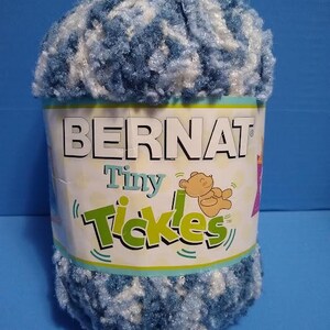 May include: A skein of Bernat Tiny Tickles yarn in a blue and white colorway. The yarn is soft and fluffy, and it is perfect for making baby blankets, hats, and other accessories.