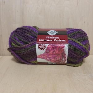 May include: A large ball of Charisma yarn in shades of purple, green, and brown. The yarn is wrapped with a label that reads "Charisma" in English, French, and Spanish. The label also features a picture of a knitted project.