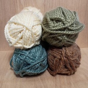 May include: Four balls of thick, chunky yarn arranged in a square formation. The top left ball is cream, the top right is sage green, the bottom left is teal blue, and the bottom right is a warm, earthy brown. Each ball features a twisted ply texture.