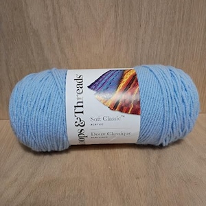 May include: A light blue yarn ball with a white label that reads "Loops & Threads Soft Classic Acrylic Doux Classique". The yarn is a soft, fluffy texture, perfect for knitting or crocheting projects.