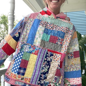 Puede incluir: Una sudadera con capucha de patchwork colorida con una capucha rosa. La sudadera está hecha de diferentes telas con patrones florales y geométricos en tonos de azul, verde, rojo, amarillo y morado.