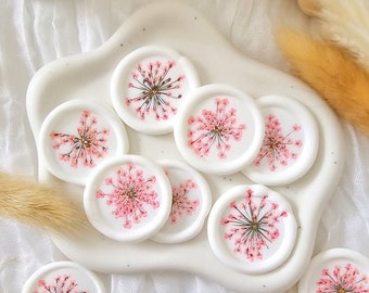 Puede incluir: Un conjunto de diez sellos de cera blanca con flores rosas prensadas en su interior. Los sellos son redondos y tienen un acabado liso y brillante.