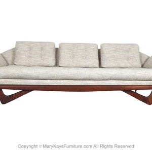 May include: A mid-century modern sofa with a light-colored fabric and a dark wood frame. The sofa features three back cushions and two arm cushions. The wooden frame has a unique angled design.