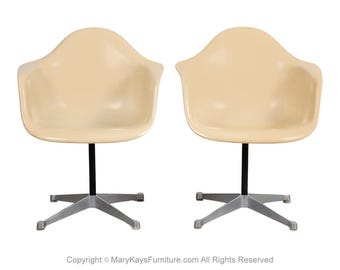 May include: Two beige swivel chairs with black bases and silver star-shaped legs. The chairs are made of molded plastic and have a simple, modern design.