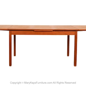 May include: A rectangular wooden dining table with a warm reddish-brown finish. The table has a central section and two drop-leaf extensions. The table is supported by four straight legs.