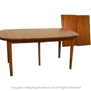 May include: A wooden oval dining table with two leaf extensions. The table is made of a rich brown wood and has a simple, elegant design.
