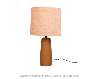 May include: A brown ceramic table lamp with a carved design and a beige linen lampshade.