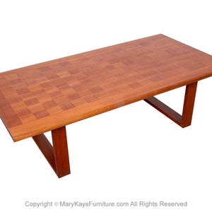 May include: A rectangular wooden coffee table with a checkered pattern on the top and a simple, modern design. The table has a light brown finish and is made of solid wood.