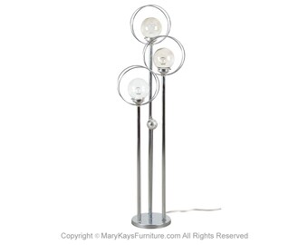 May include: A chrome floor lamp with three round glass shades. The lamp has a modern design with three circular rings.