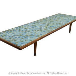 May include: A long, rectangular coffee table with a mosaic tile top in shades of blue, green, and white. The table has a dark wood frame and four tapered legs. The table is approximately 60 inches long.