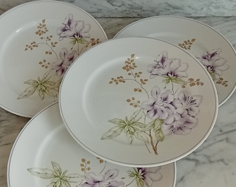 May include: Four white ceramic dinner plates with a floral design featuring purple flowers and green leaves. The plates have a gold rim.