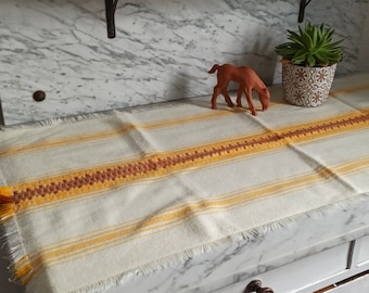 May include: A white and yellow striped table runner with a fringed edge. The runner is on a marble countertop with a small brown horse figurine and a potted succulent plant.