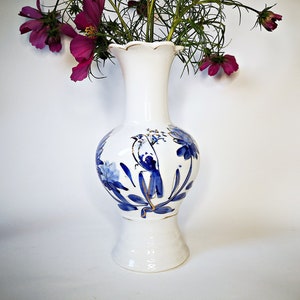 May include: A white porcelain vase with a blue and gold floral design. The vase has a scalloped rim and a round base.