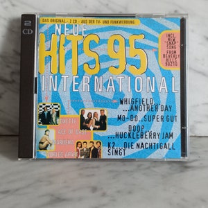 Pode incluir: Um conjunto de dois CDs intitulado "Neue Hits 95 International" com um fundo listrado azul, amarelo e preto. A capa apresenta uma colagem de imagens de vários artistas, incluindo Ace of Base, Whigfield e Mo-Do. O texto "Incl. New "Snap" Song From Beverly Hills 90210" está em um retângulo rosa no canto superior direito.