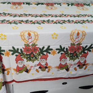 Può includere: Tovaglia bianca con un design natalizio rosso e verde. Il design presenta un motivo ripetitivo di candele, agrifoglio e gnomi. La tovaglia ha un bordo rosso e bianco.