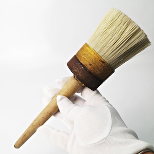 Könnte beinhalten: Ein Bürste mit einem langen, dünnen Holzstiel und einem runden, weißen Borstenkopf. Die Bürste ist mit einem gelben und braunen Band umwickelt.