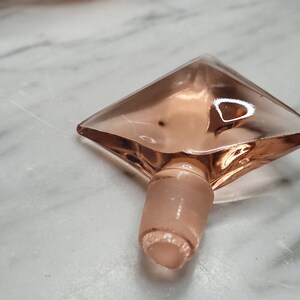May include: A pink glass bottle stopper shaped like a diamond with a rounded bottom.