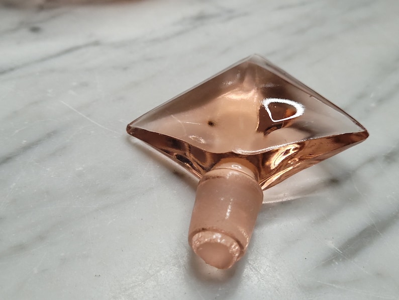 May include: A pink glass bottle stopper shaped like a diamond with a rounded bottom.