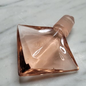May include: A pink glass bottle stopper with a diamond-shaped base and a round top.
