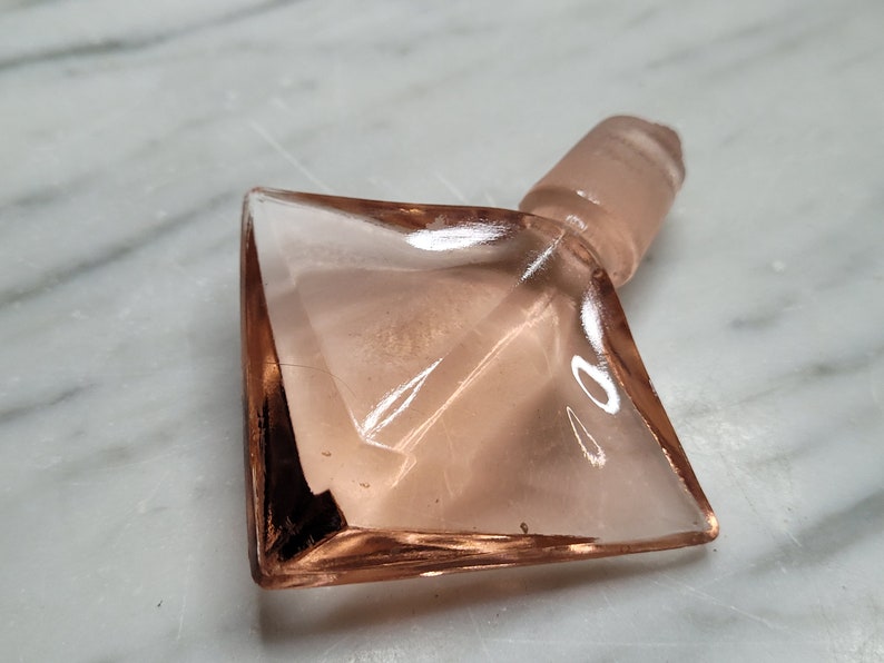 May include: A pink glass bottle stopper with a diamond-shaped base and a round top.