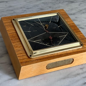 May include: A vintage wooden barometer with a gold-coloured metal frame and a black face. The barometer has a rectangular shape and features a dial with numbers and needles. The wooden base has a rectangular shape with a mesh detail.