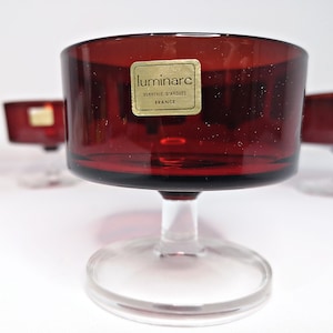 Könnte beinhalten: Set aus vier roten Glasschalen mit klaren Glasstielen und -sockeln. Die Schalen haben ein goldenes Etikett mit der Aufschrift "luminarc verrerie d'arques france".