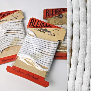 May include: Three spools of white rope labelled "BLEIBAND" with red and tan packaging. The packaging includes "70 Gramm" and "25 m". A close-up shows the texture of the white rope.